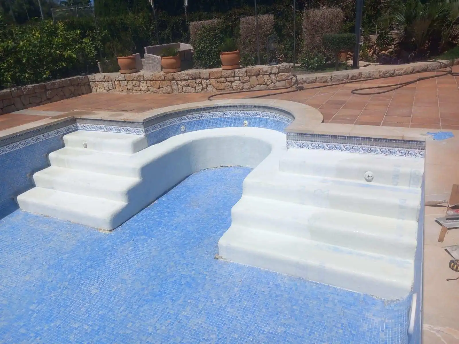 Piscina con revestimiento de gresite azul y escalera romana de obra con barandilla metálica en Mallorca