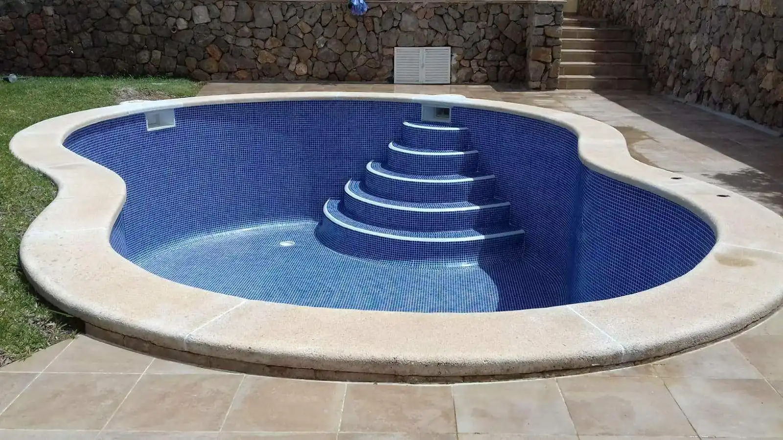 Piscina con revestimiento de gresite azul y escalera romana de obra con barandilla metálica en Mallorca