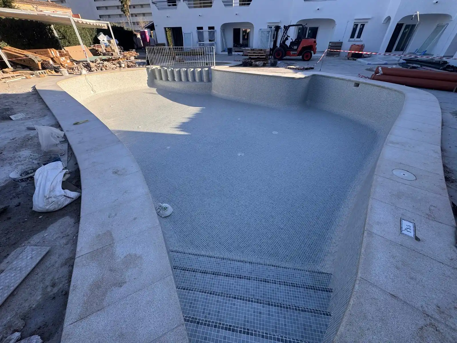 Construcción de piscina con revestimiento de gresite gris y coronación de piedra en Palma
