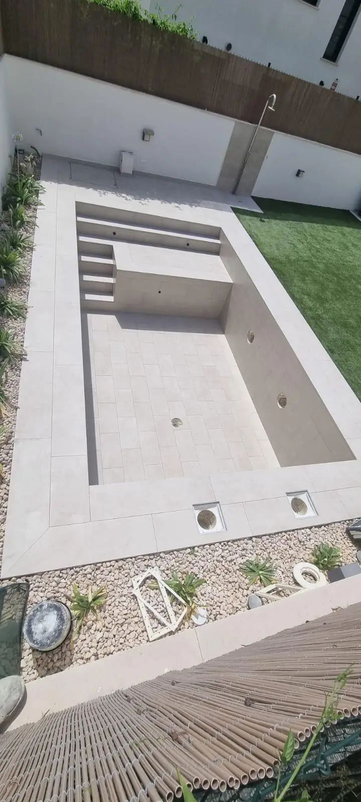 Construcción de piscina con revestimiento cerámico gris y escalera de obra integrada en Palma
