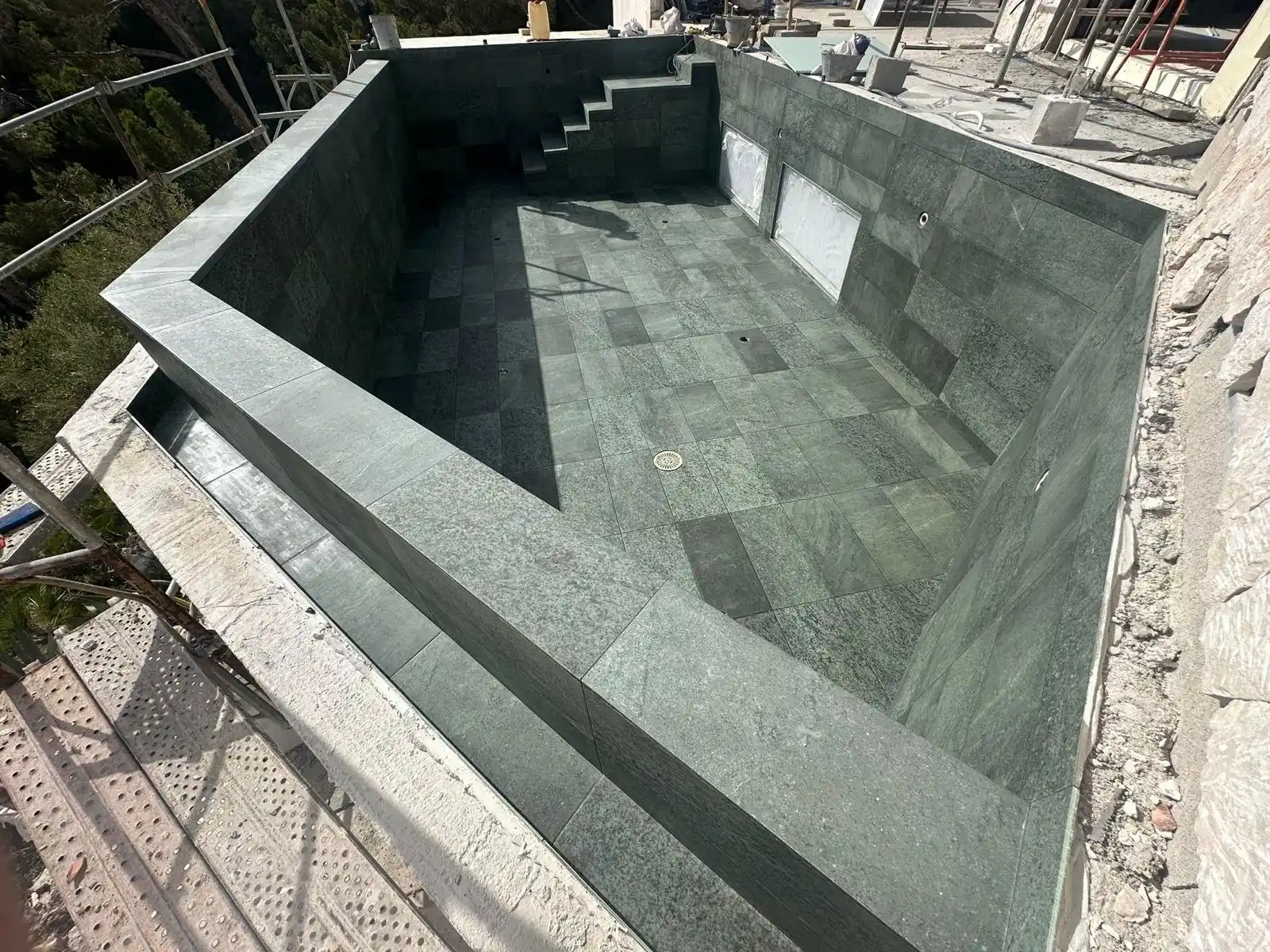 Construcción de piscina con revestimiento de piedra natural verde y escaleras integradas en Palma